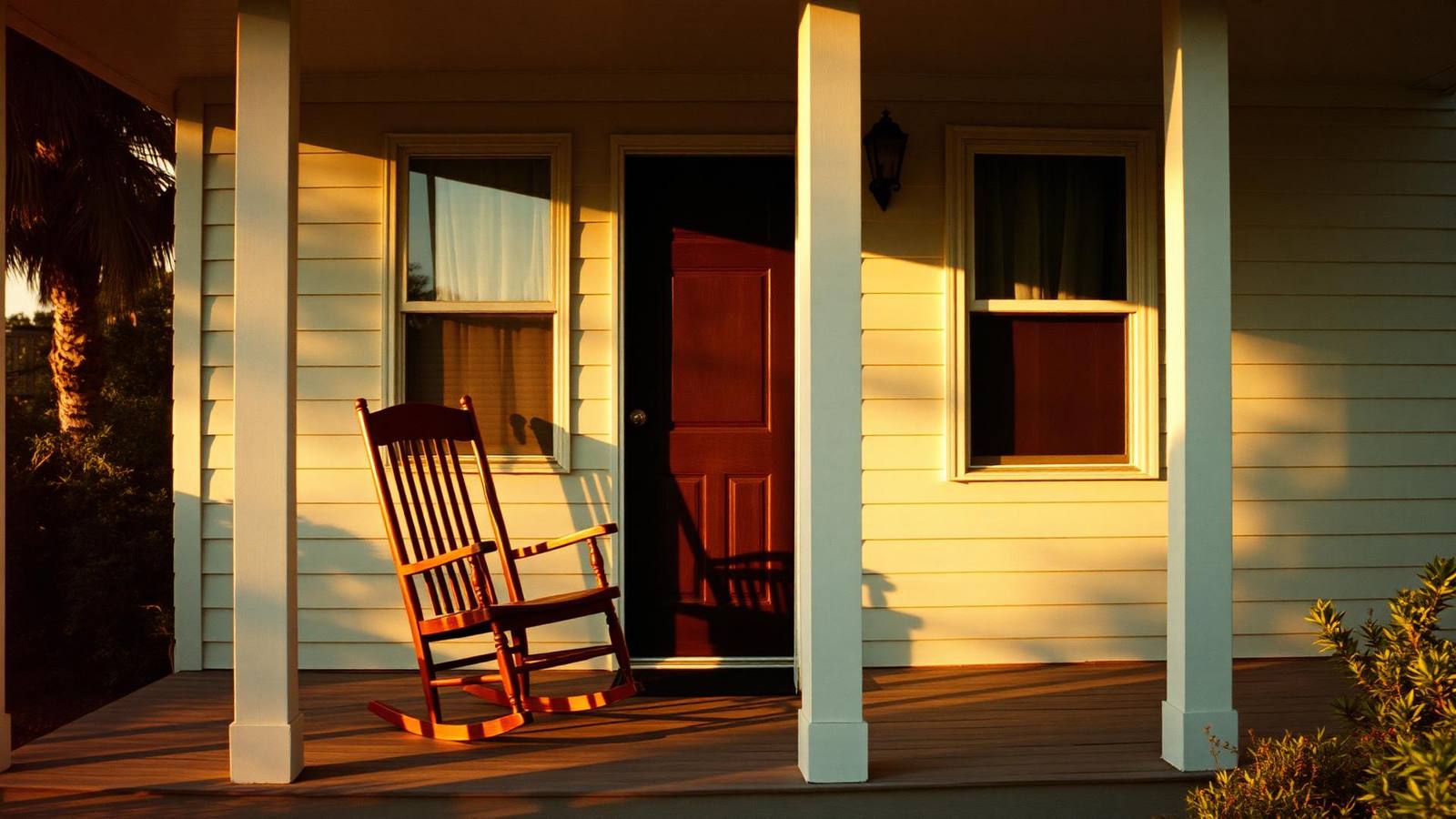 The porch of an older Kissimmee bungalow in late afternoon light, a wooden rocking chair beside a screen door