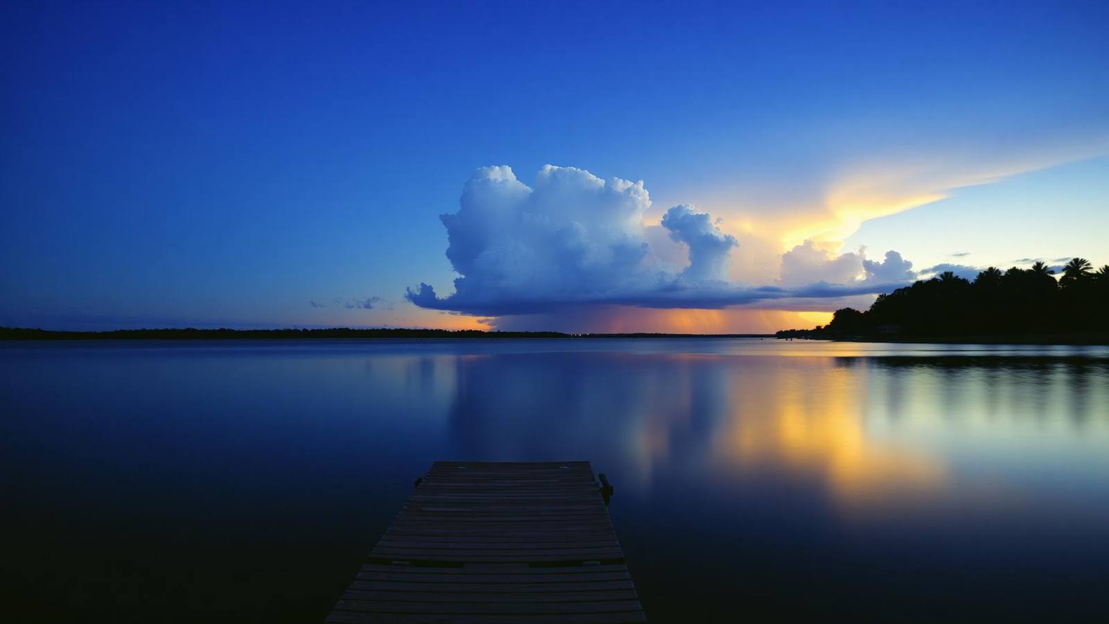 A wooden dock on a Lake Mary lake at dusk, an evening storm building on the far shore
