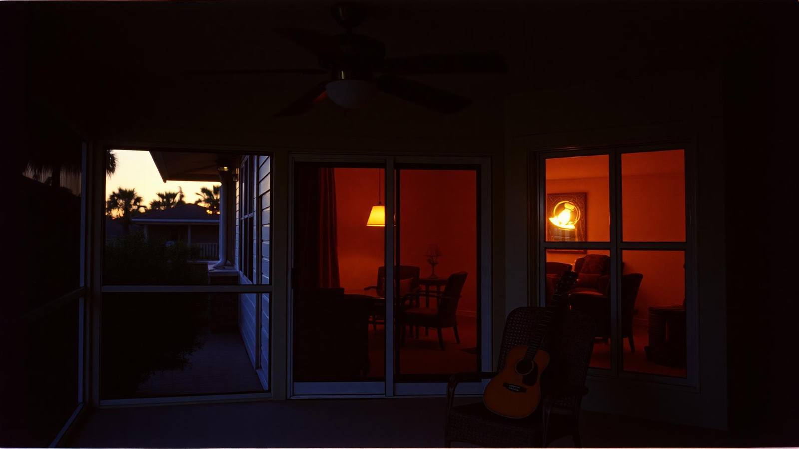 A screened Windermere lanai at dusk, ceiling fan turning, an open guitar case on a wicker chair with warm lamp light inside