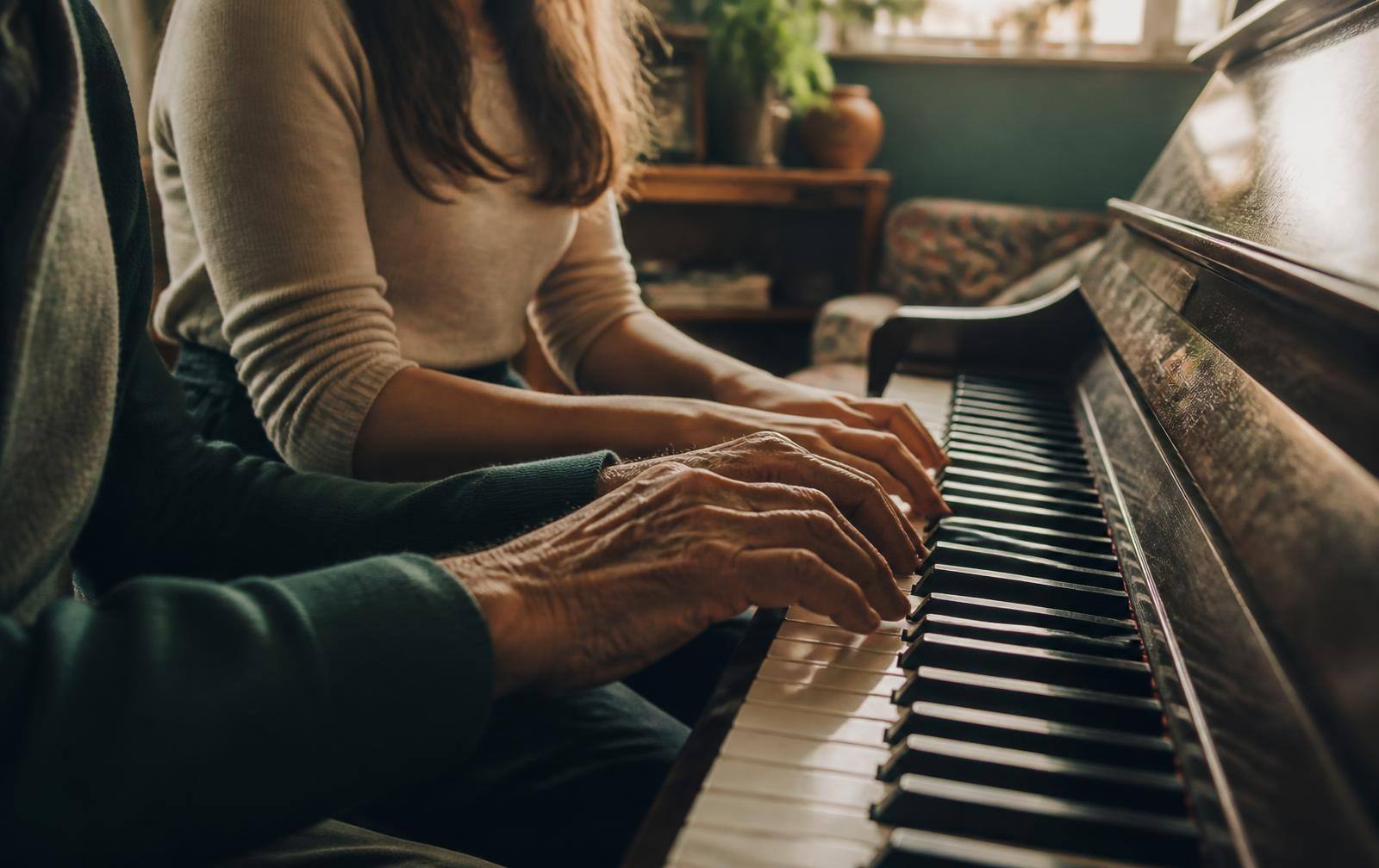Two pairs of hands, one older and one younger, playing an upright piano together